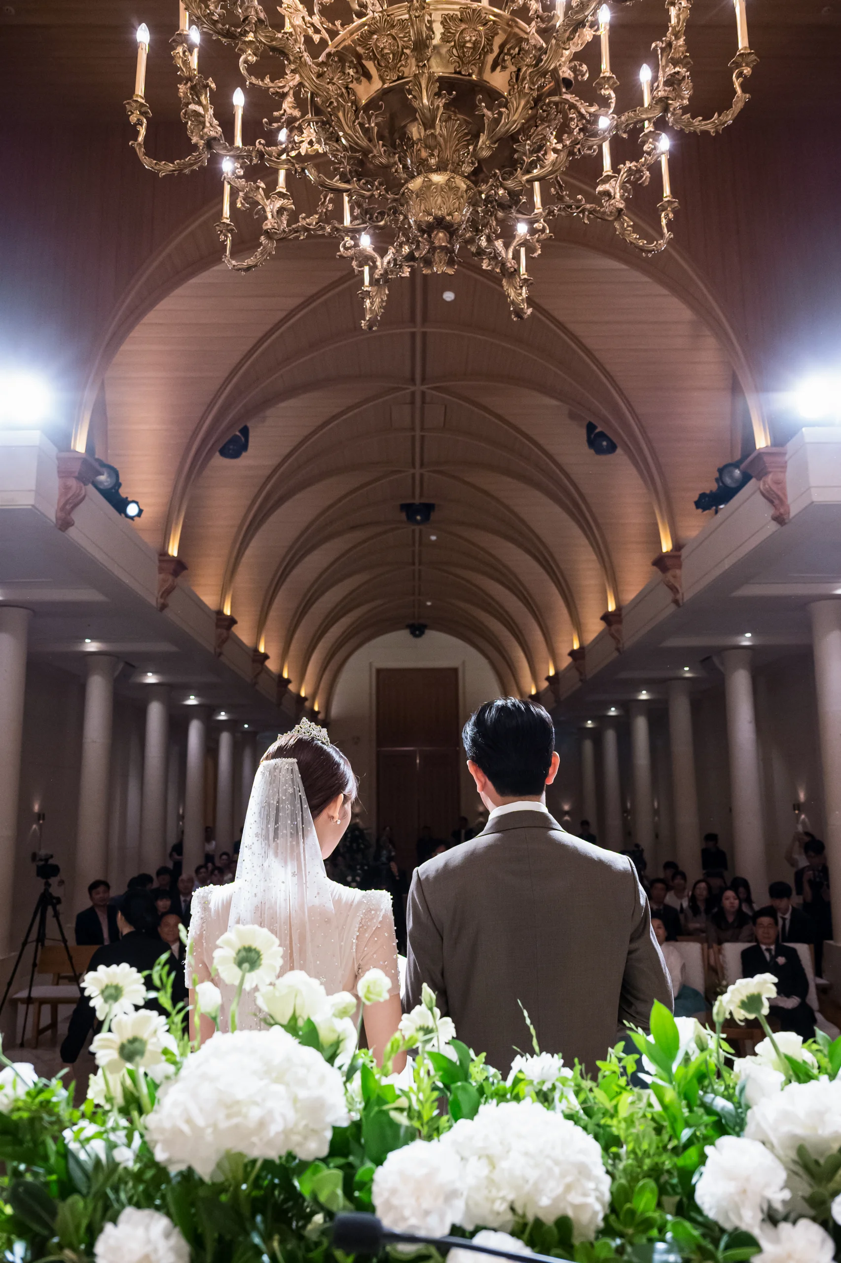 서울 공덕 아펠가모 라로브홀 결혼식사진 — 샹들리에 아래 혼인서약을 하는 신랑 신부 뒷모습