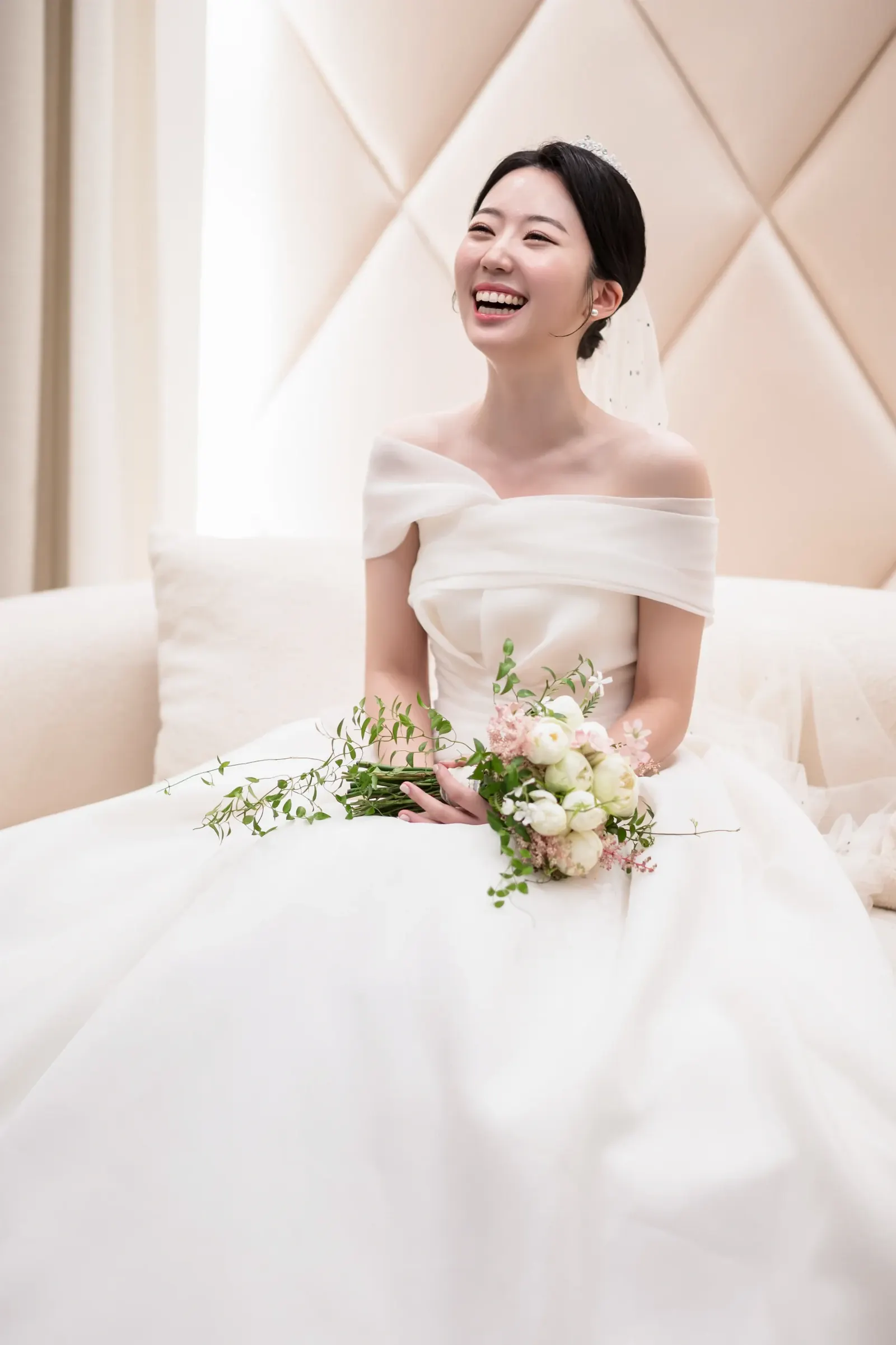 포스코컨벤션 결혼식사진 — 크림색 누빔 벽 신부대기실 소파에서 부케를 들고 활짝 웃는 신부