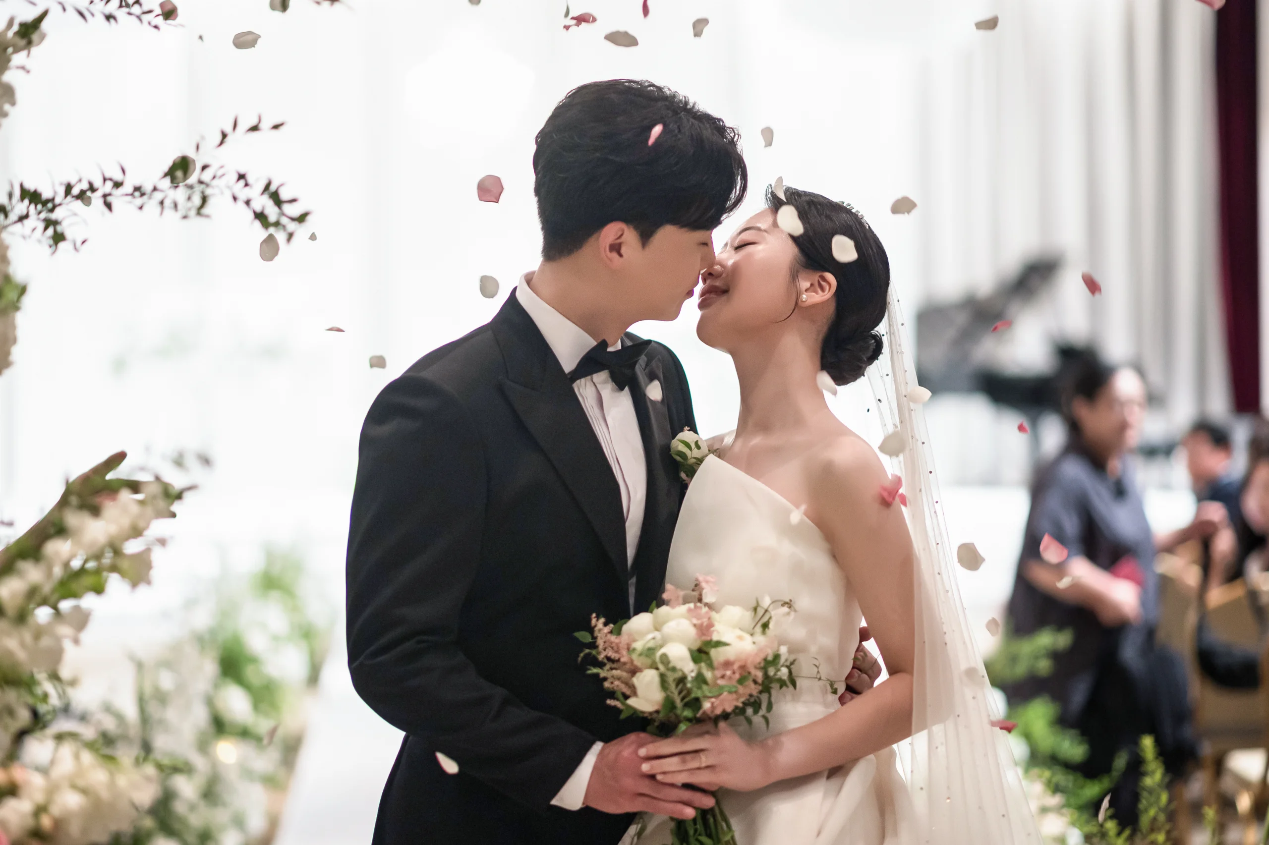 서울 포스코컨벤션 결혼식사진 — 꽃잎이 흩날리는 예식장에서 입맞춤하는 신랑 신부