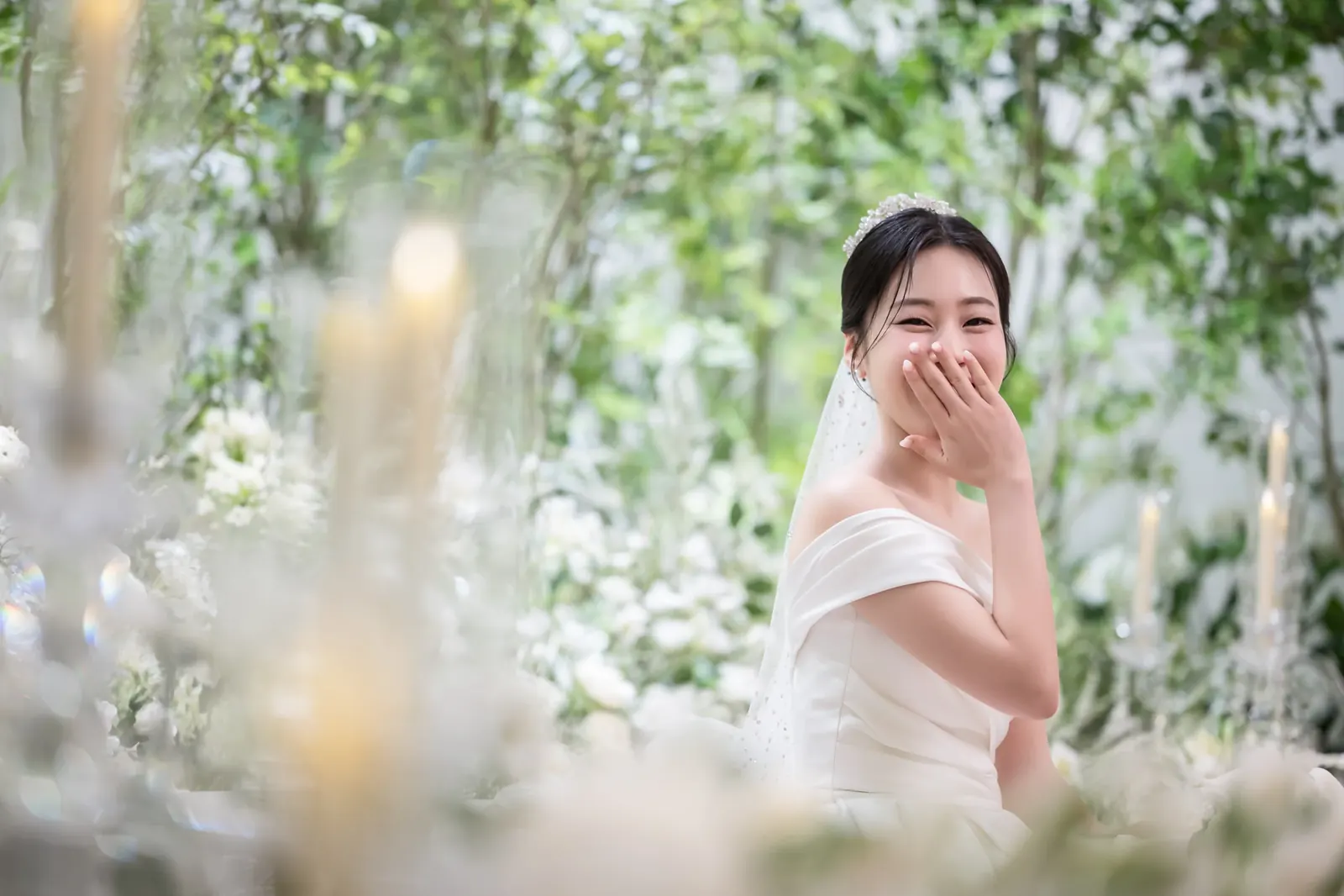 세인트메리엘 결혼식사진 — 흐린 흰 꽃 너머로 입을 가리고 웃는 신부
