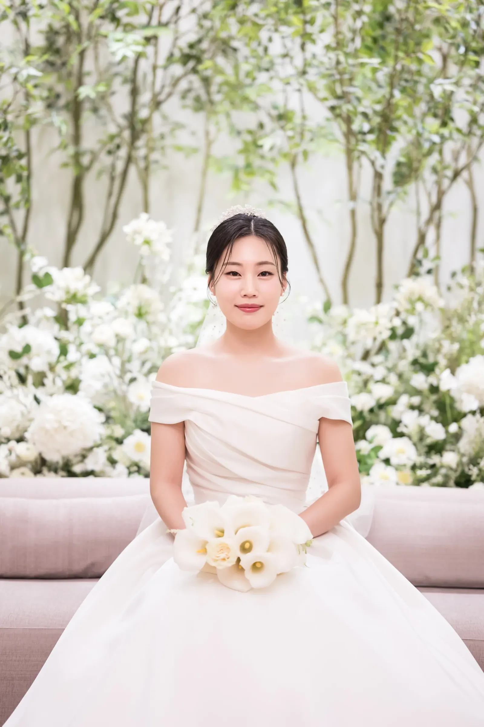 세인트메리엘 결혼식사진 — 나무와 흰 꽃장식 대기실 소파에 칼라 부케를 들고 앉은 신부