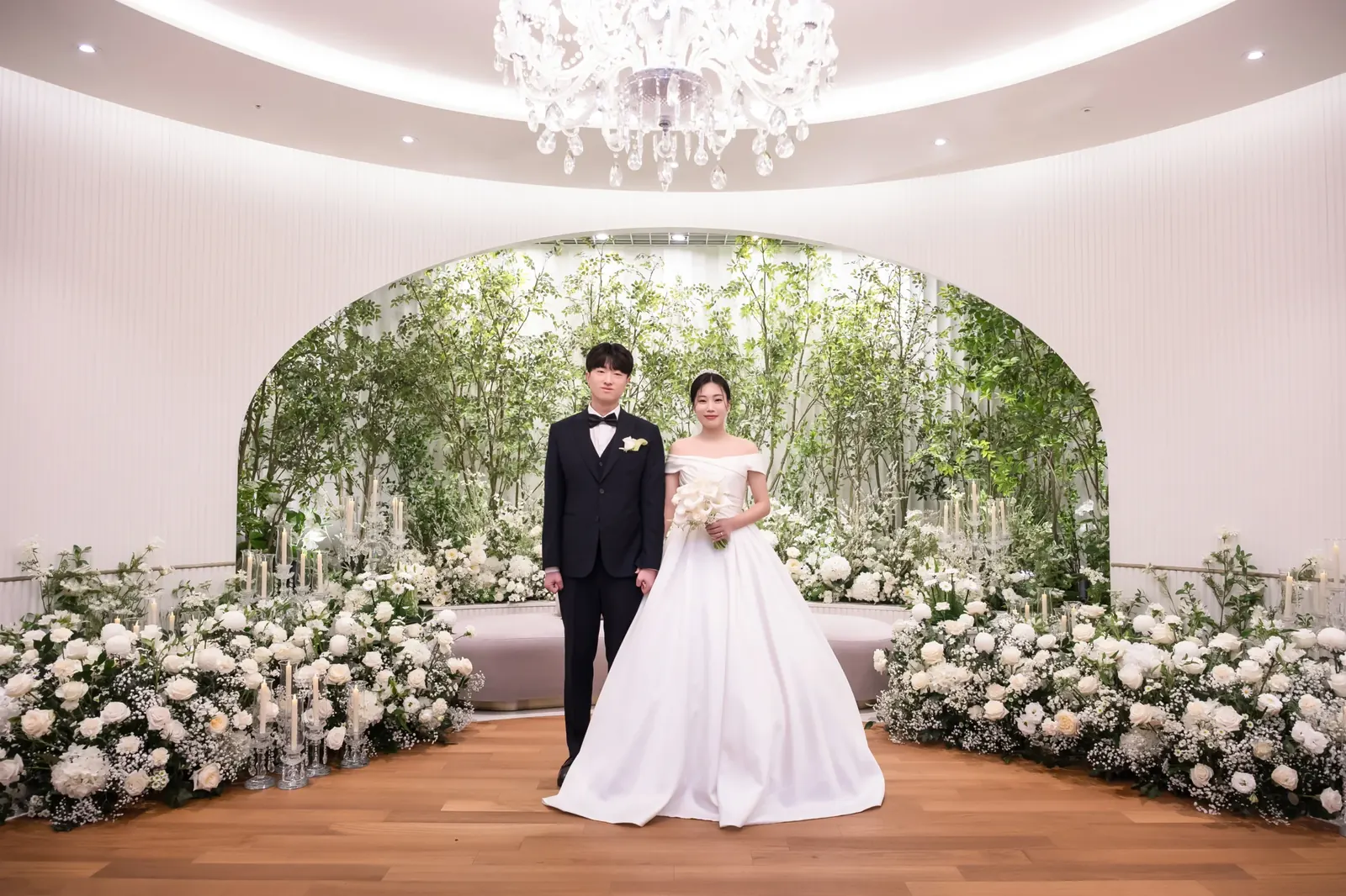 정원 분위기의 결혼식사진 — 서울 강남구 세인트메리엘 실내 홀, 나무와 초록 아치 장식 앞 나무 바닥에 선 신랑 신부