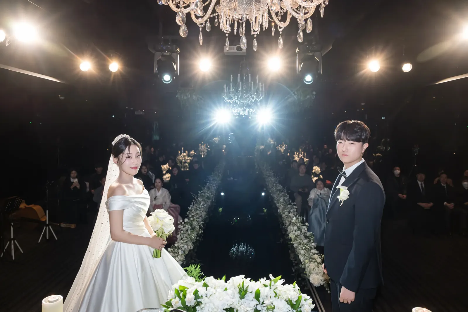 세인트메리엘 결혼식사진 — 무대 조명이 비추는 어두운 단상 앞에 선 신랑 신부