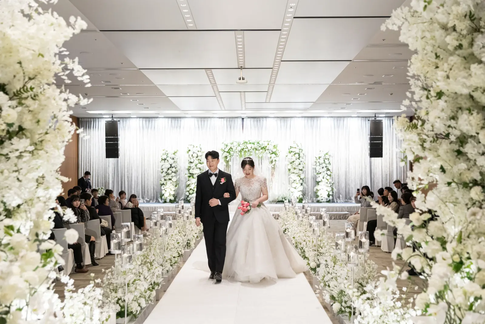 행진 사진 예시 — 서울 강동구 삼성E&A 흰 꽃 장식 버진로드를 천천히 걸어 나오는 신랑 신부와 하객