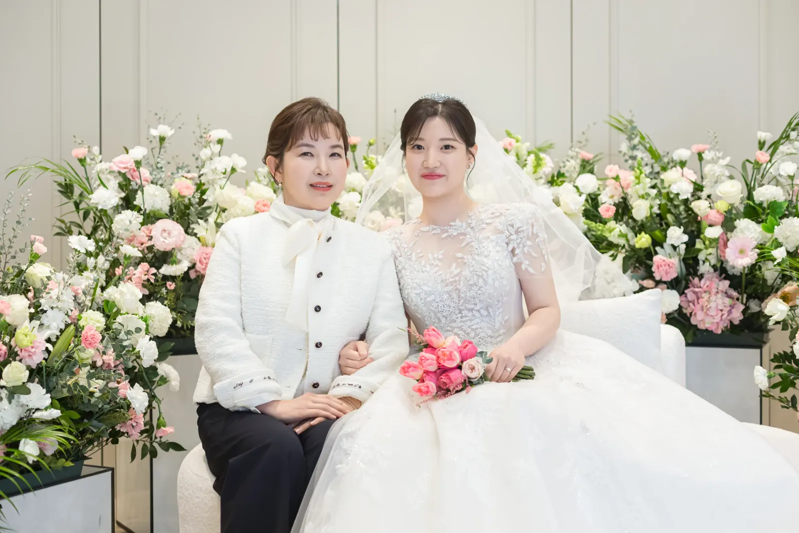 신부대기실 결혼식사진 — 서울 강동구 삼성E&A 꽃장식 소파에 흰 재킷 차림 하객과 나란히 앉은 신부