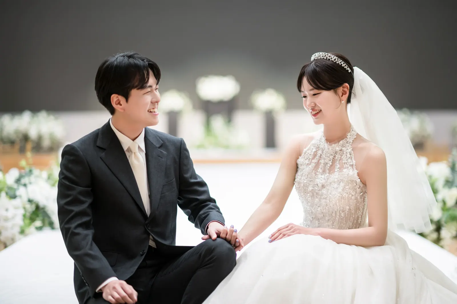 스몰웨딩 분위기의 결혼식사진 — 서울 서초구 삼성금융캠퍼스 단상 끝에 나란히 앉아 서로를 보며 웃는 신랑 신부