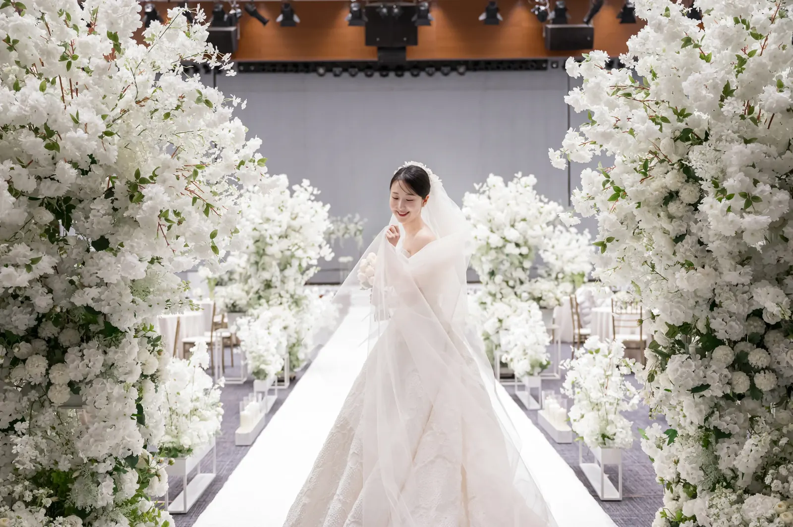삼성서초사옥 결혼식사진 — 흰 꽃나무 사이 버진로드를 걸어 들어오며 웃는 신부