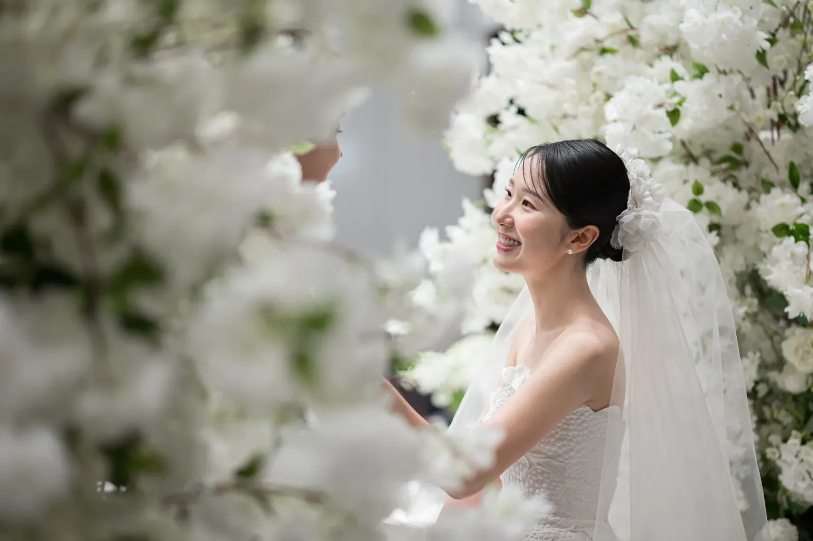 삼성서초사옥 결혼식사진 — 흰 꽃 사이로 보이는 웃는 신부 옆모습