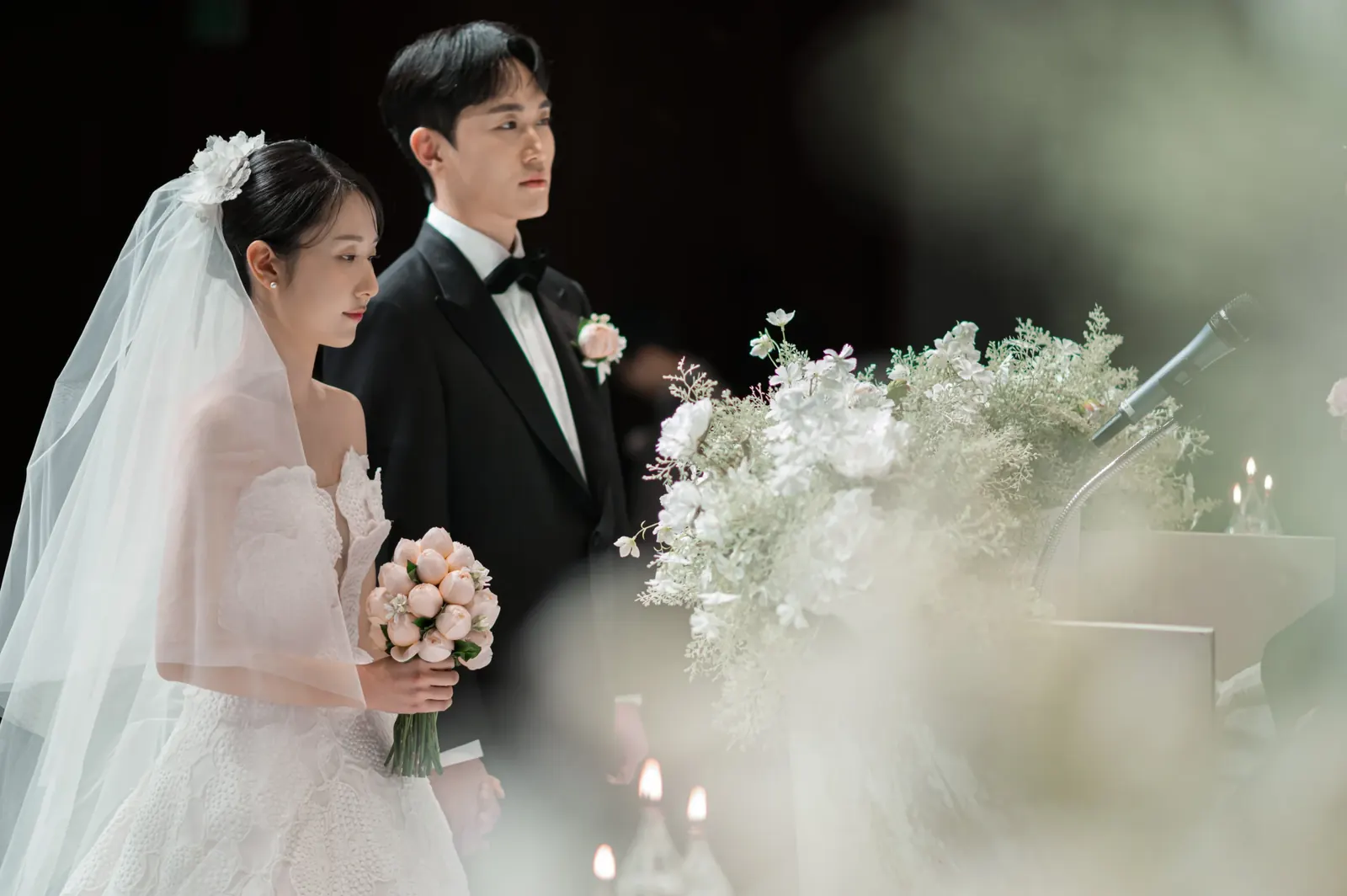 삼성서초사옥 결혼식사진 — 흐린 꽃 너머로 보이는 나란히 선 신랑 신부 옆모습