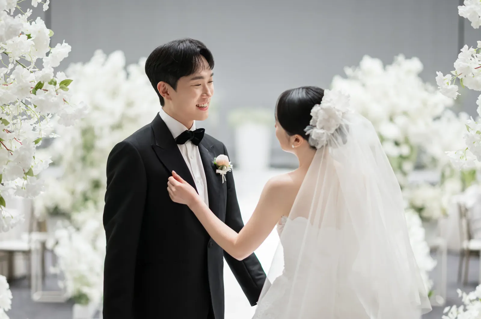 삼성서초사옥 결혼식사진 — 흰 꽃장식 앞에서 신랑 가슴에 손을 얹고 마주 선 신부