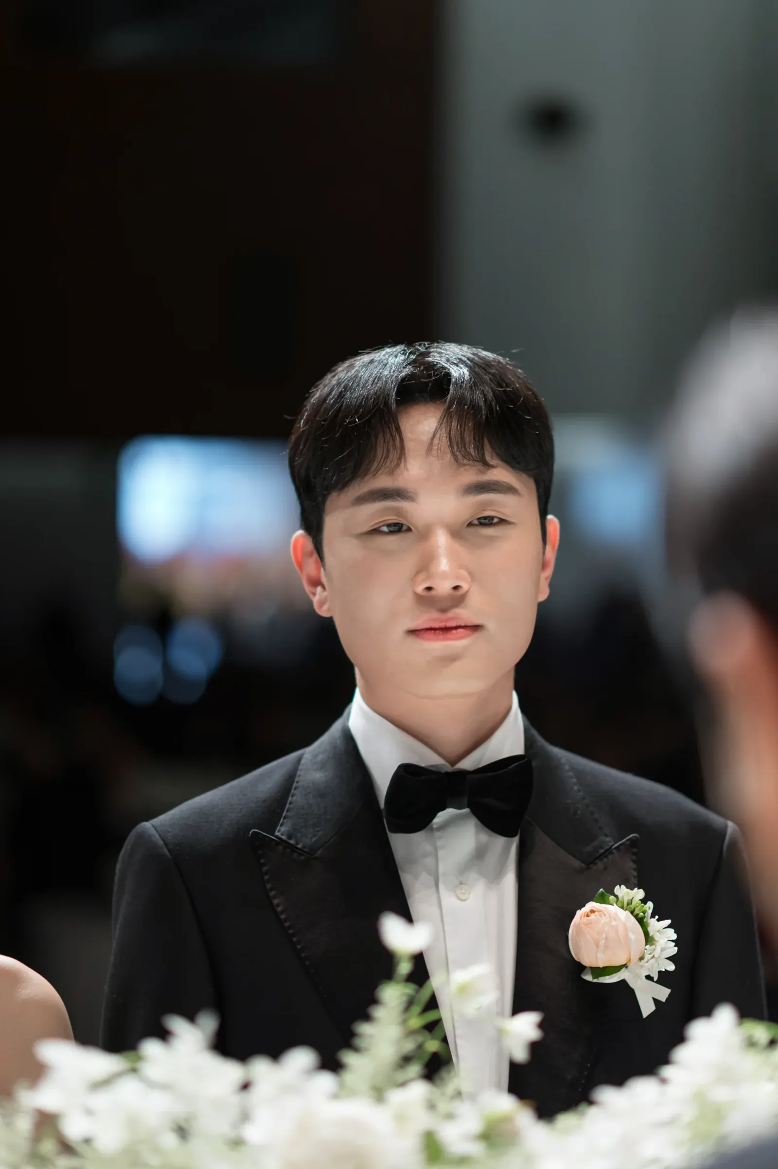 삼성서초사옥 결혼식사진 — 단상 앞 흰 꽃 너머로 담은 신랑 얼굴 클로즈업