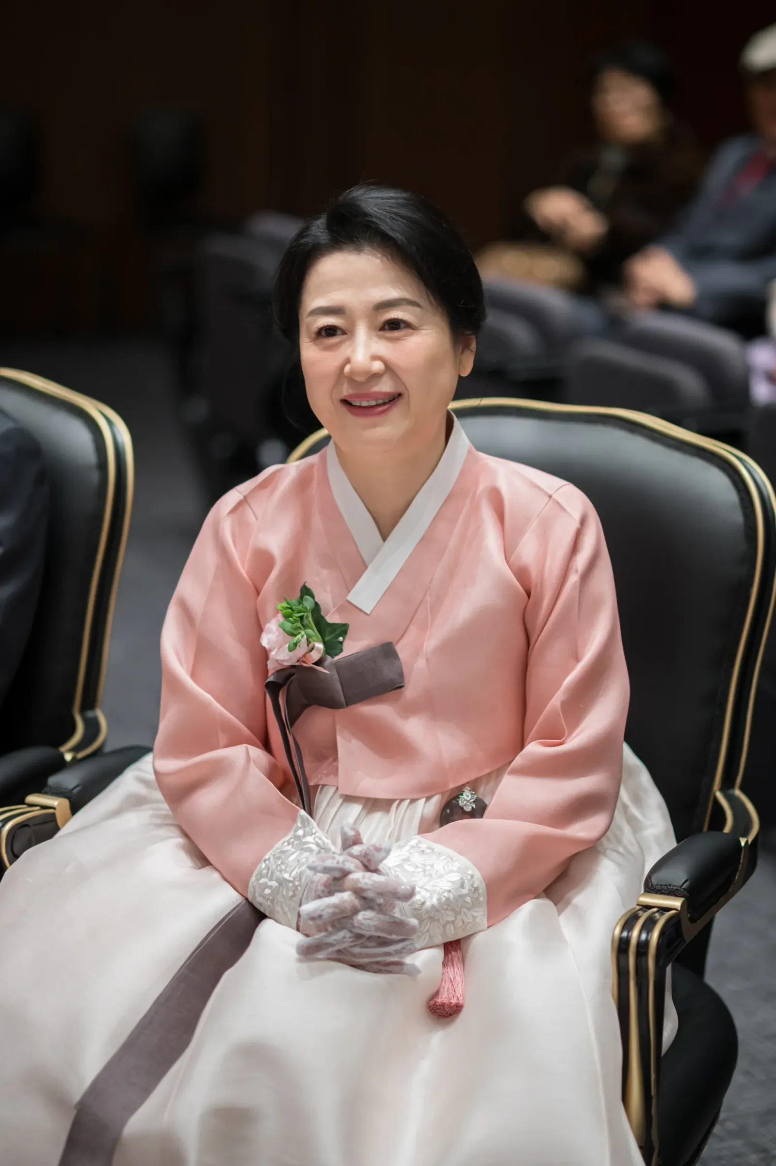 결혼식 가족사진 — 서울 서초구 삼성서초사옥 혼주석에서 분홍 한복을 입고 두 손을 모은 채 미소 짓는 어머니
